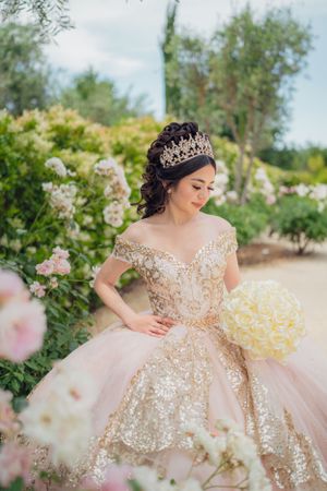 Blush pink ball gown with gold details photographed in a blooming garden setting.