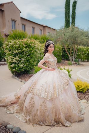 Champagne colored quinceañera dress with gold embellishments photographed in front of a Spanish style building.