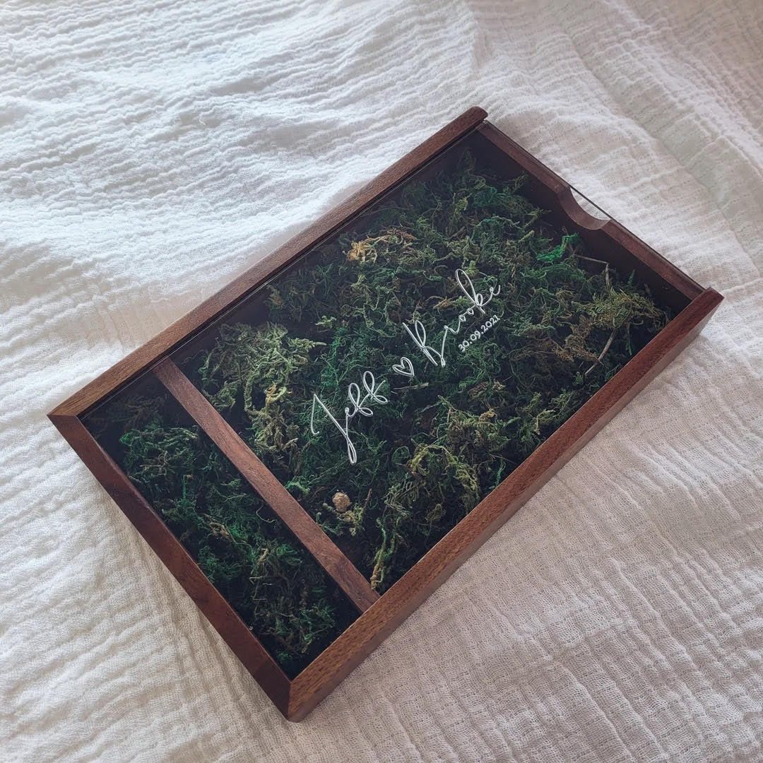 A wooden tray filled with preserved moss and greenery with cursive text.