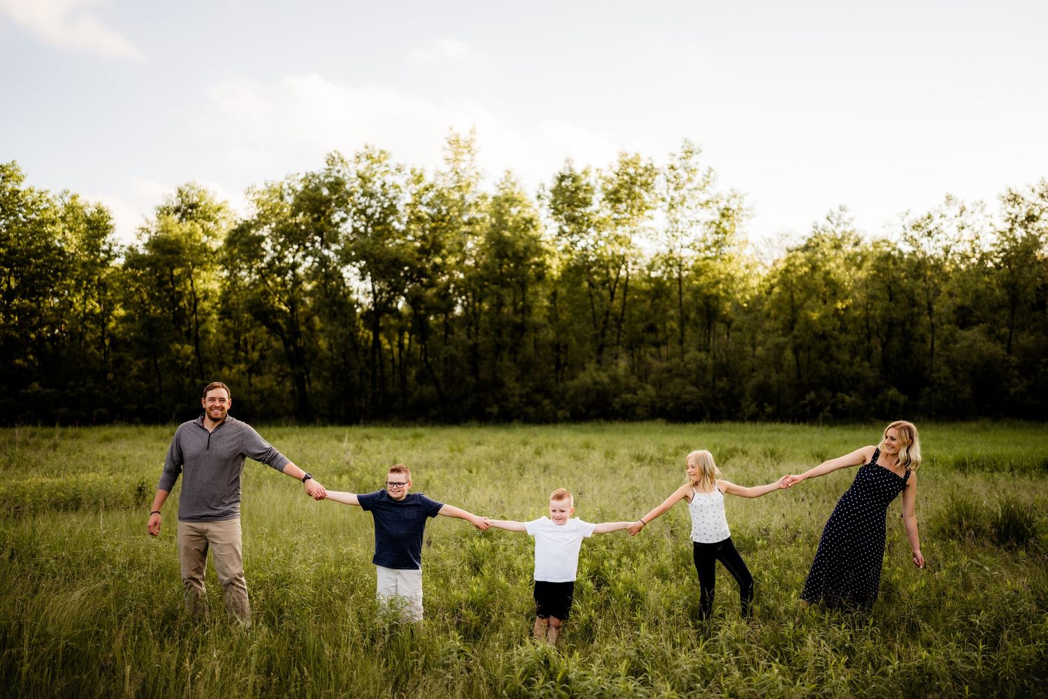 Family holding hands in a line across a grassy field at sunset.