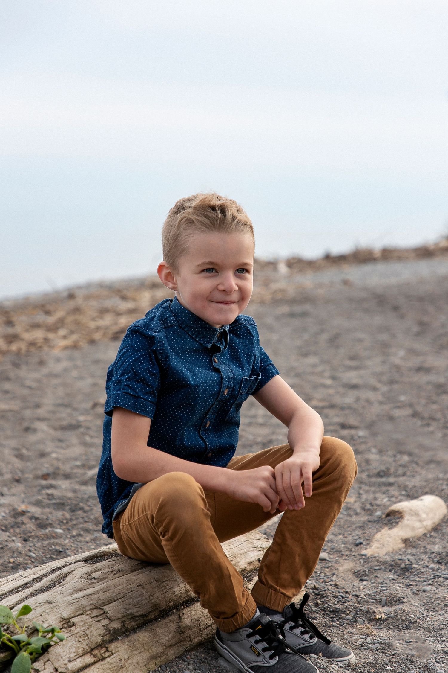 A boy sitting on a log at the beach with his arms leaning on his knees