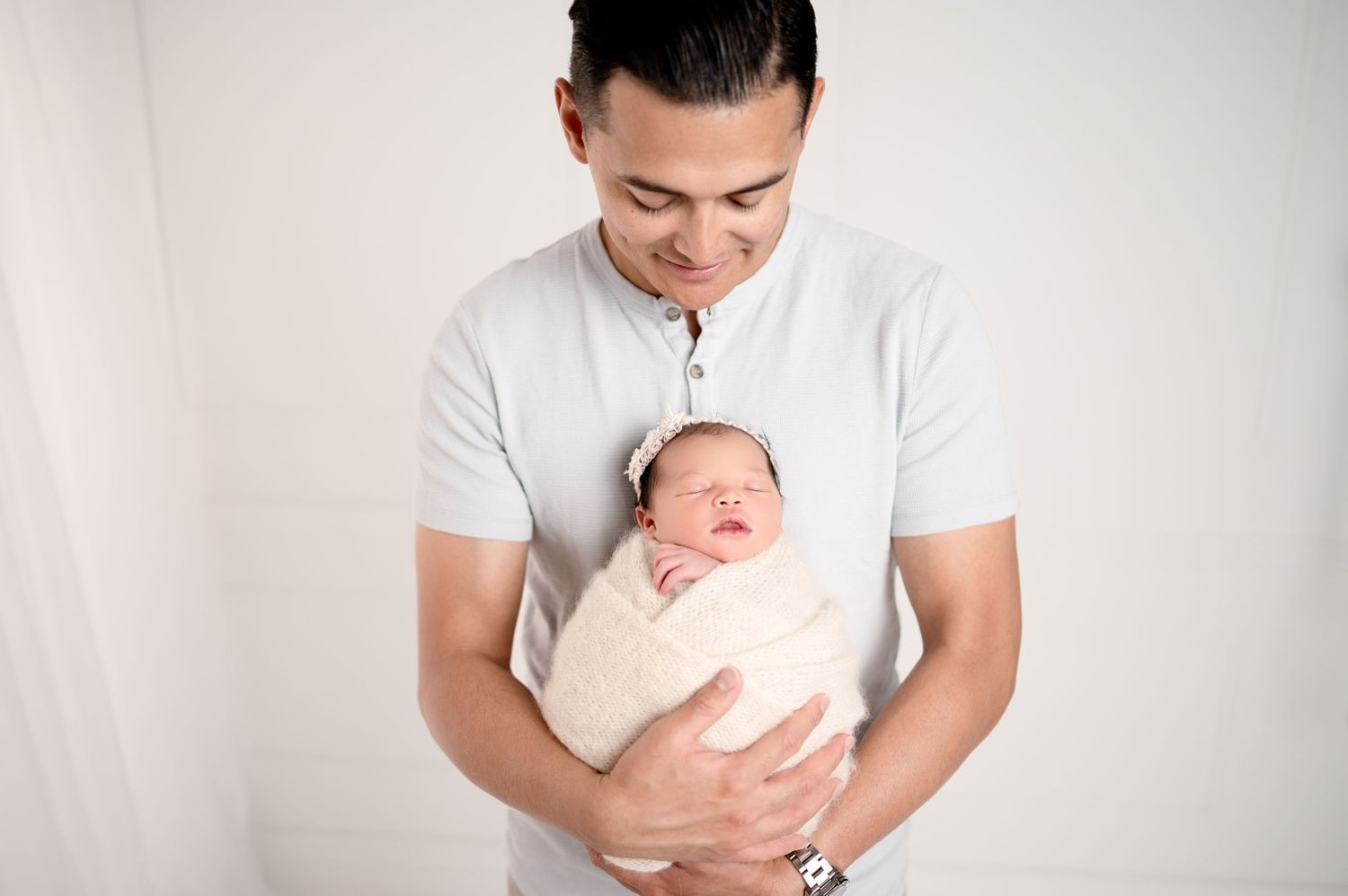 Parent in white shirt gently holding swaddled newborn against light background.