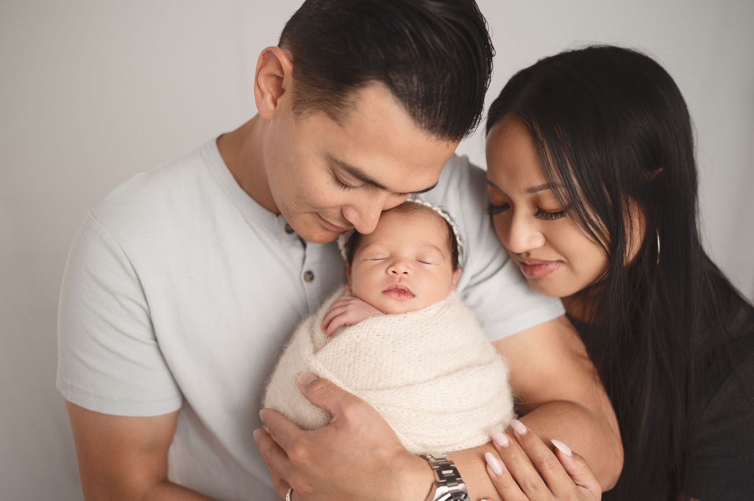 Parents lovingly embrace their swaddled newborn in intimate family portrait.
