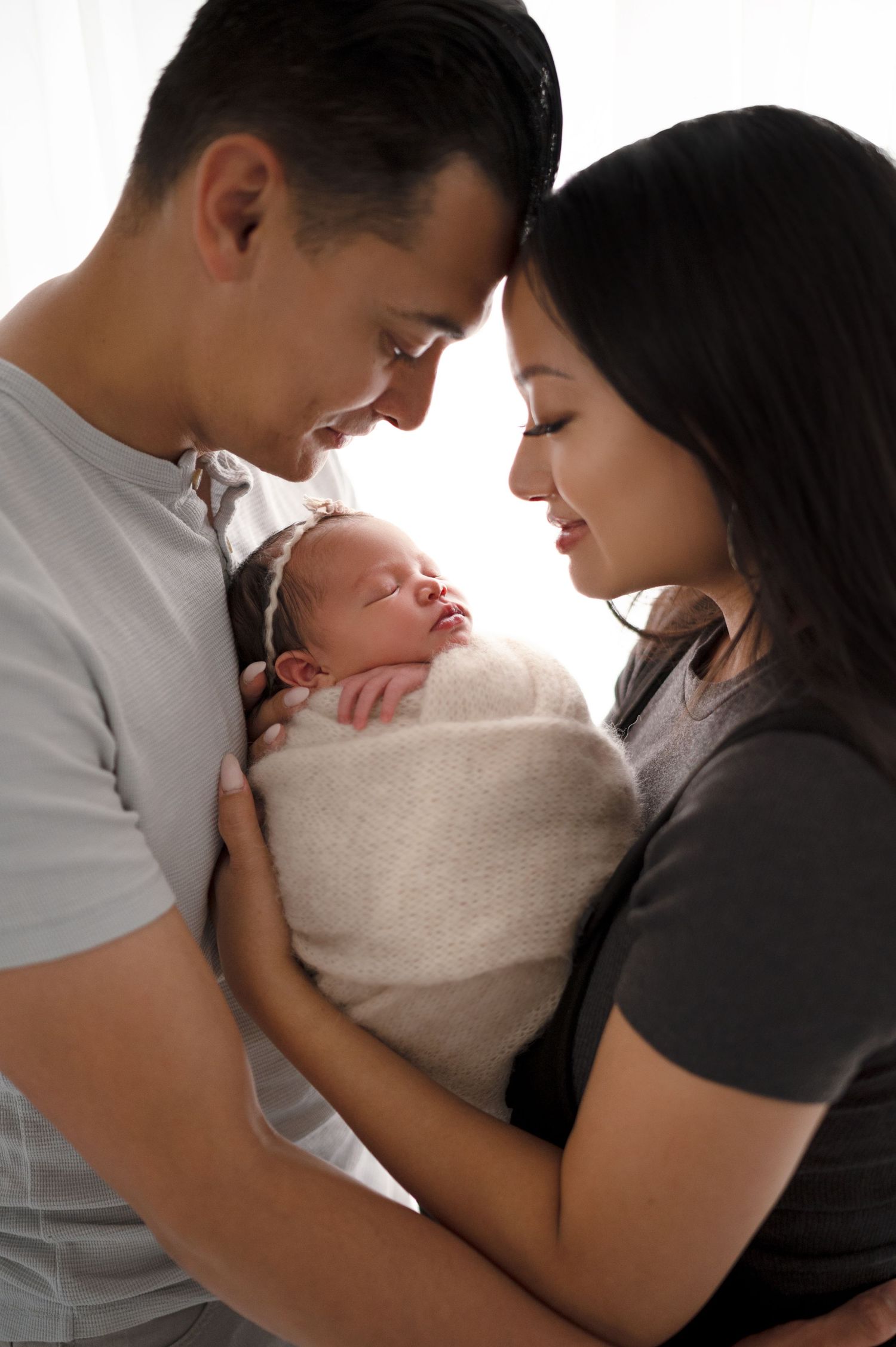 Intimate family portrait of parents gazing at their sleeping swaddled newborn.