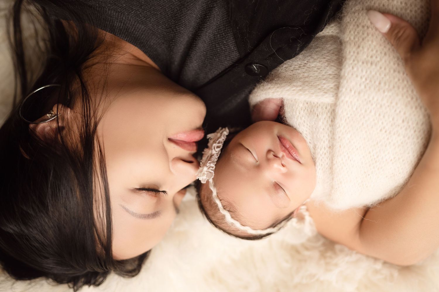 Mother lying down face-to-face with swaddled newborn wearing lace headband.