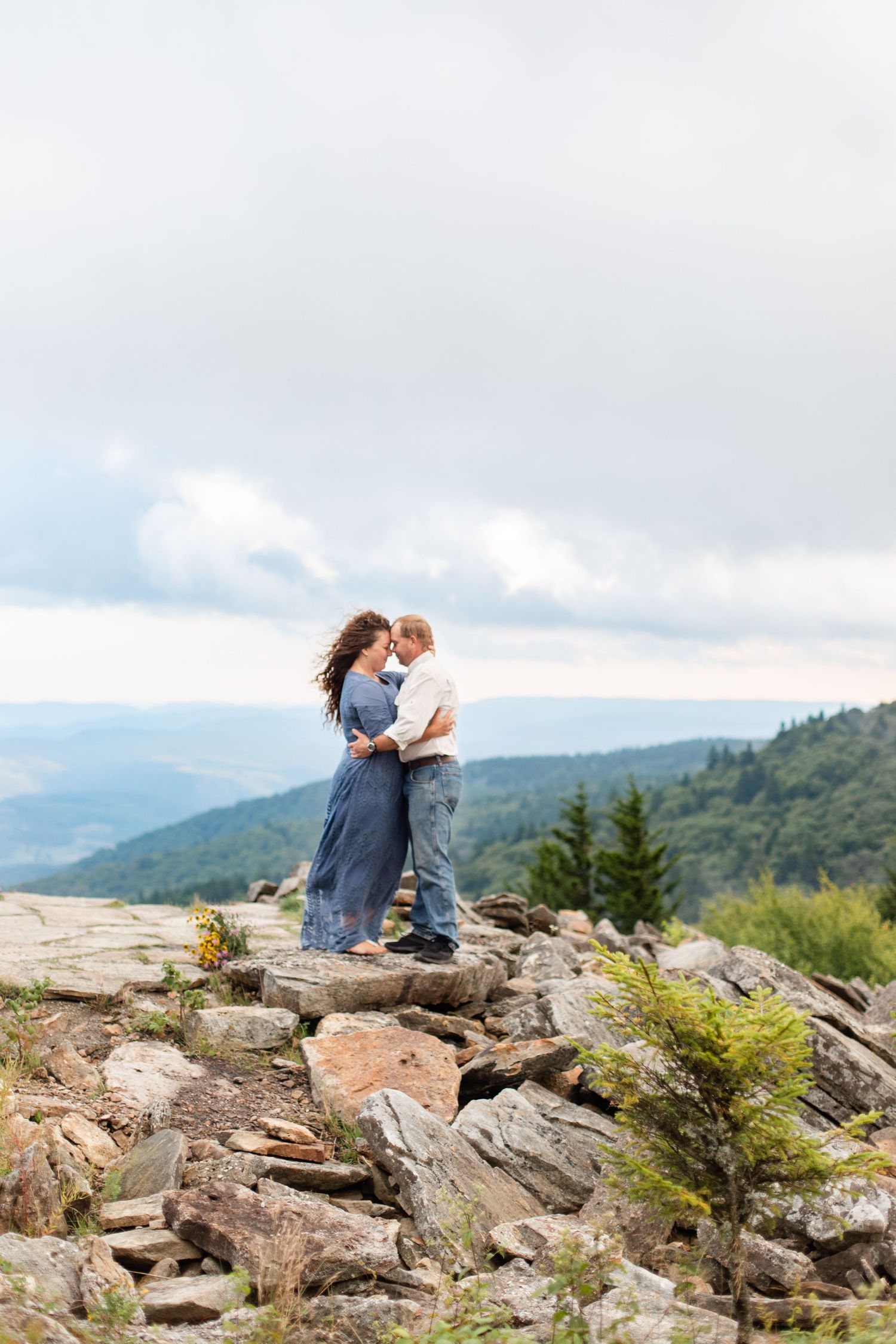 Couple sits together on rocky mountain outcrop overlooking scenic valley vista.
