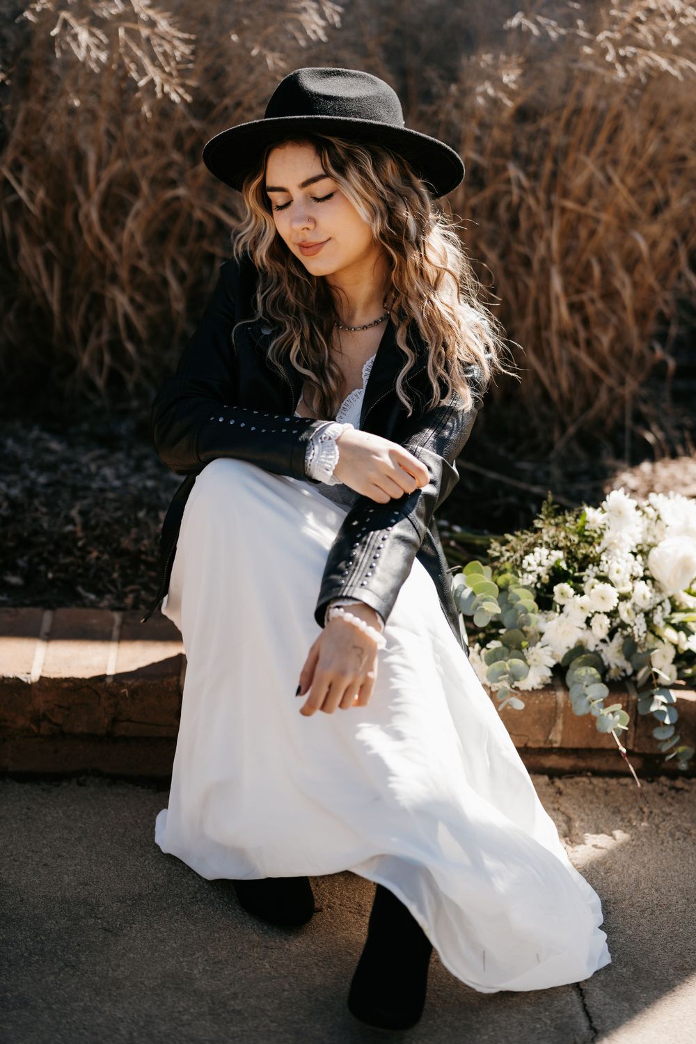 Bohemian fashion portrait with black hat and white dress against rustic outdoor background and white flowers.