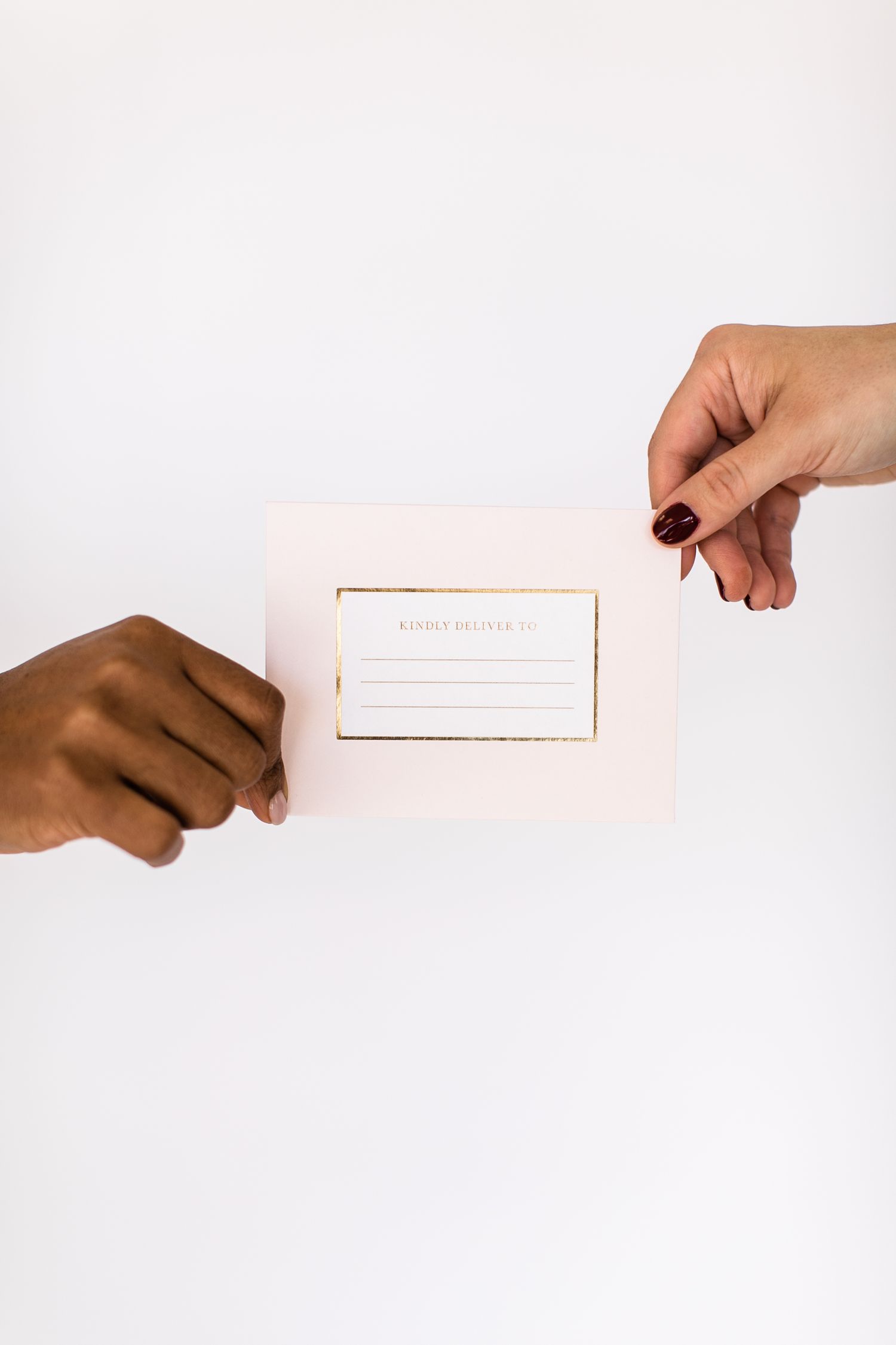 Two hands exchanging a minimalist rose gold business card against white background.