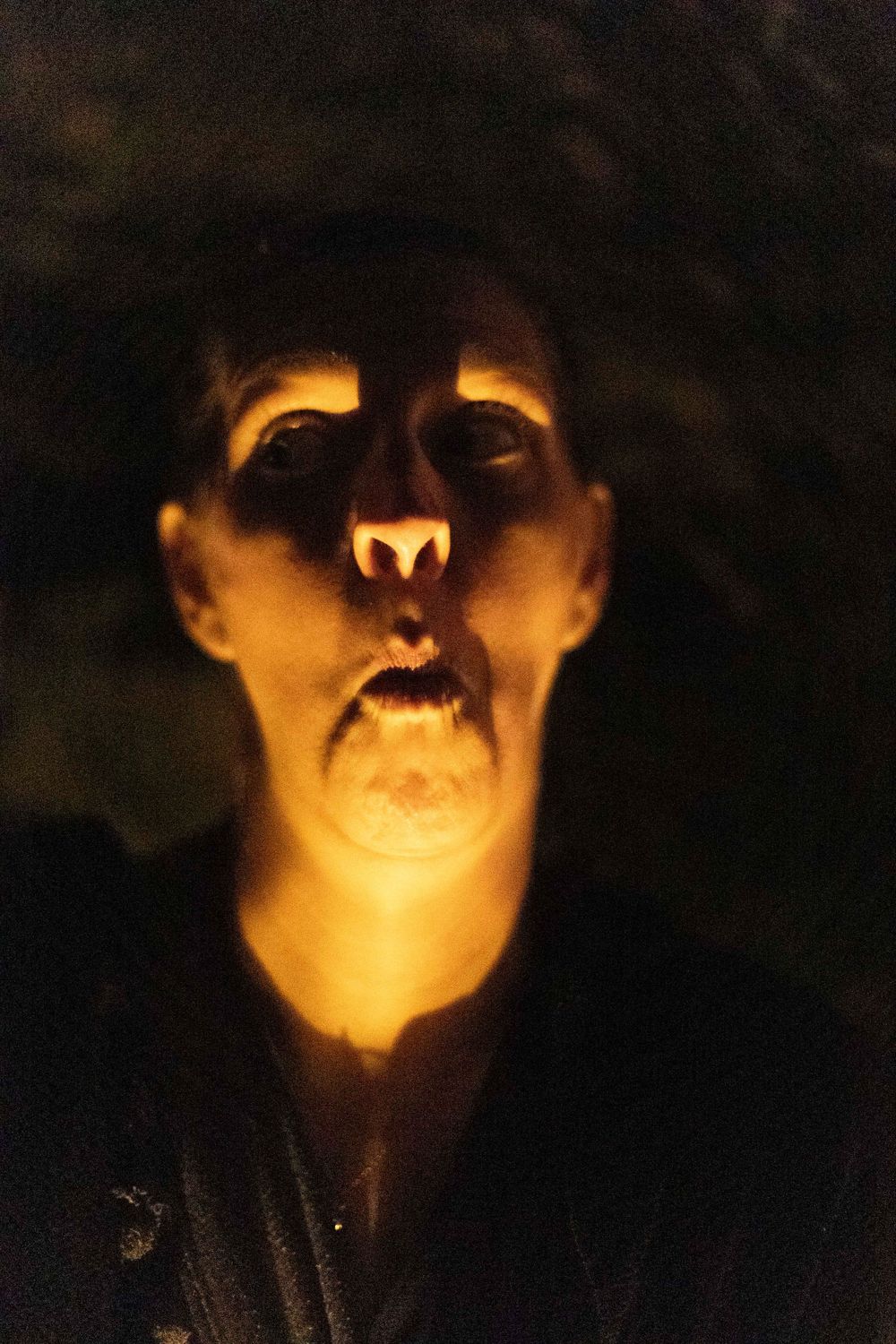 An artistic portrait lit dramatically from below by warm candlelight.