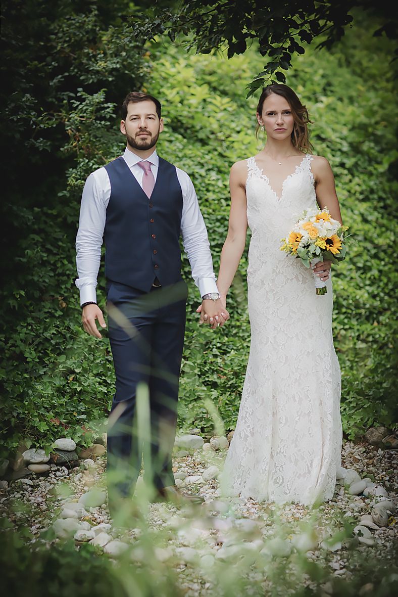 Wedding couple holding hands while standing in lush green garden setting.