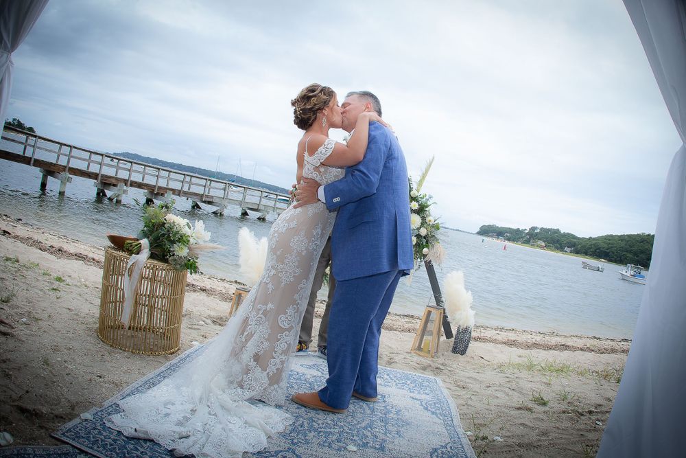 Beach wedding ceremony with couple embracing under an archway by the ocean.