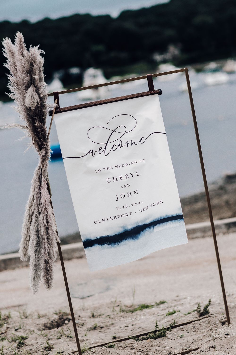 Wedding welcome sign with watercolor design displayed on beach with pampas grass decoration.