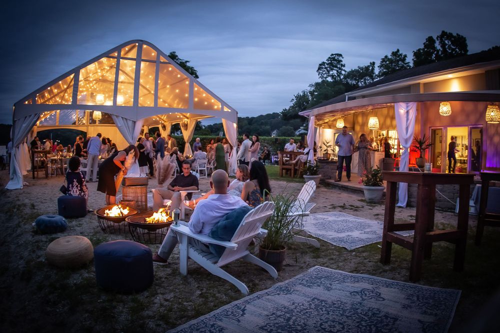 Evening wedding reception with lit barn venue and guests gathered outdoors.