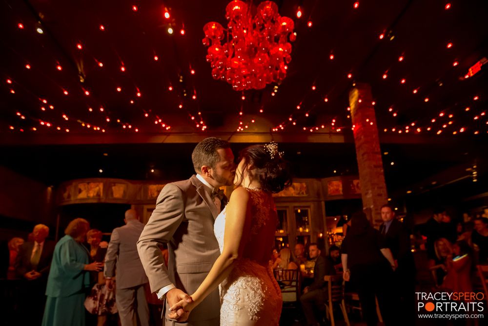 Romantic wedding couple shares a kiss under dramatic red lighting and chandeliers on their special day.