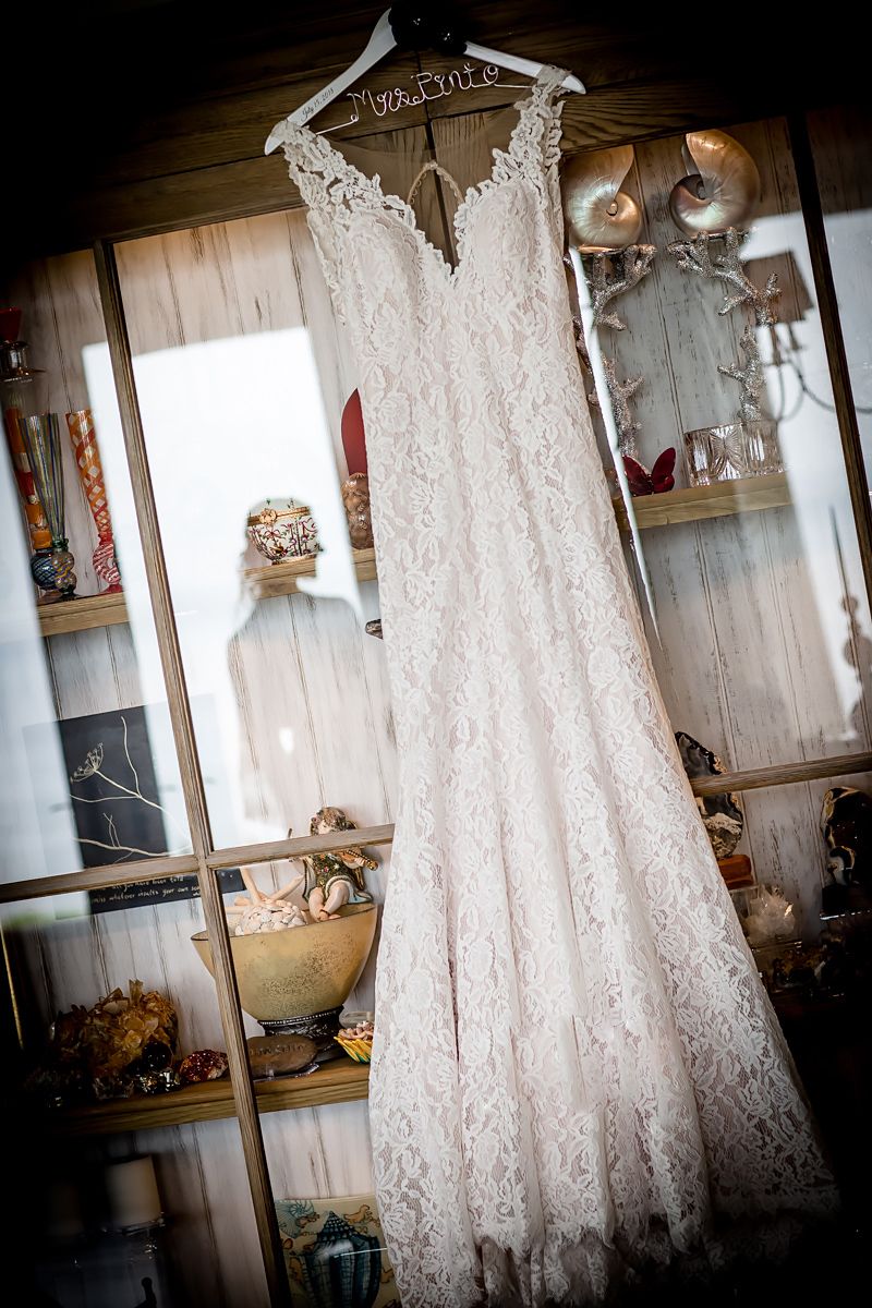 Elegant lace wedding dress hanging on display with jewelry and decor.