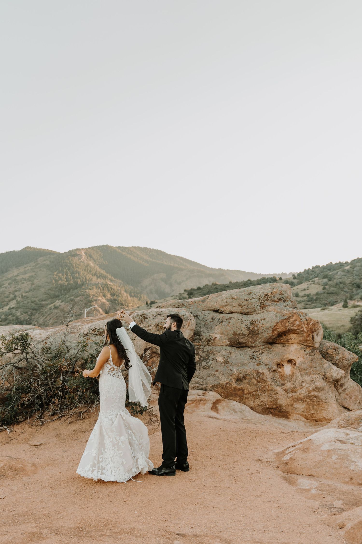 Newlyweds dance together on a scenic desert overlook during their wedding photoshoot.