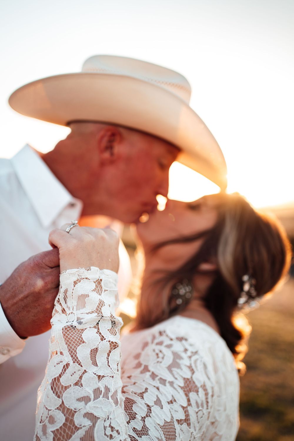 Romantic sunset portrait of couple in western attire with lace and cowboy hat details.