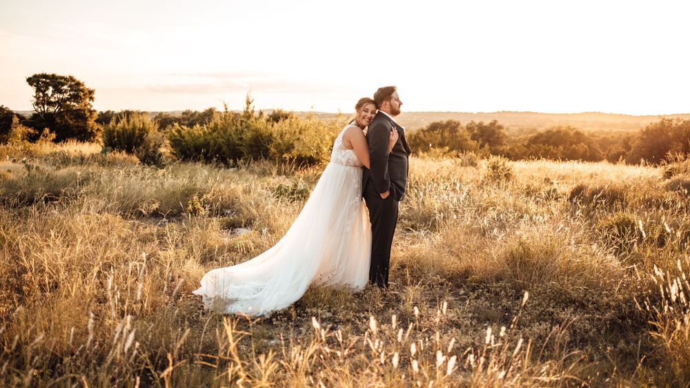 Newlyweds embrace in golden field during sunset portrait session.