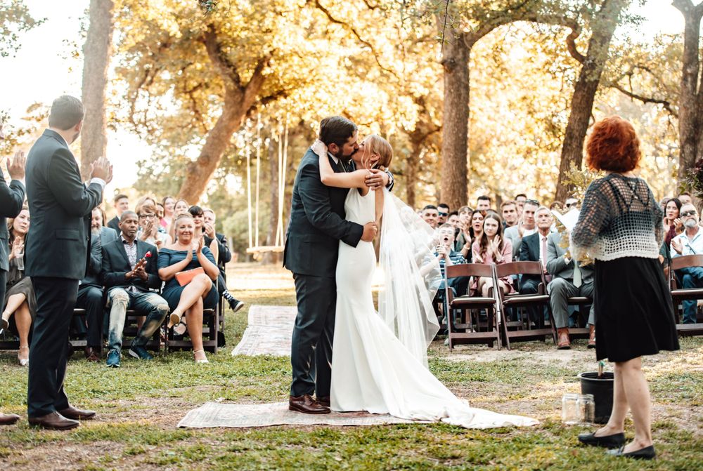 Outdoor wedding ceremony setup with guests seated under autumn trees.