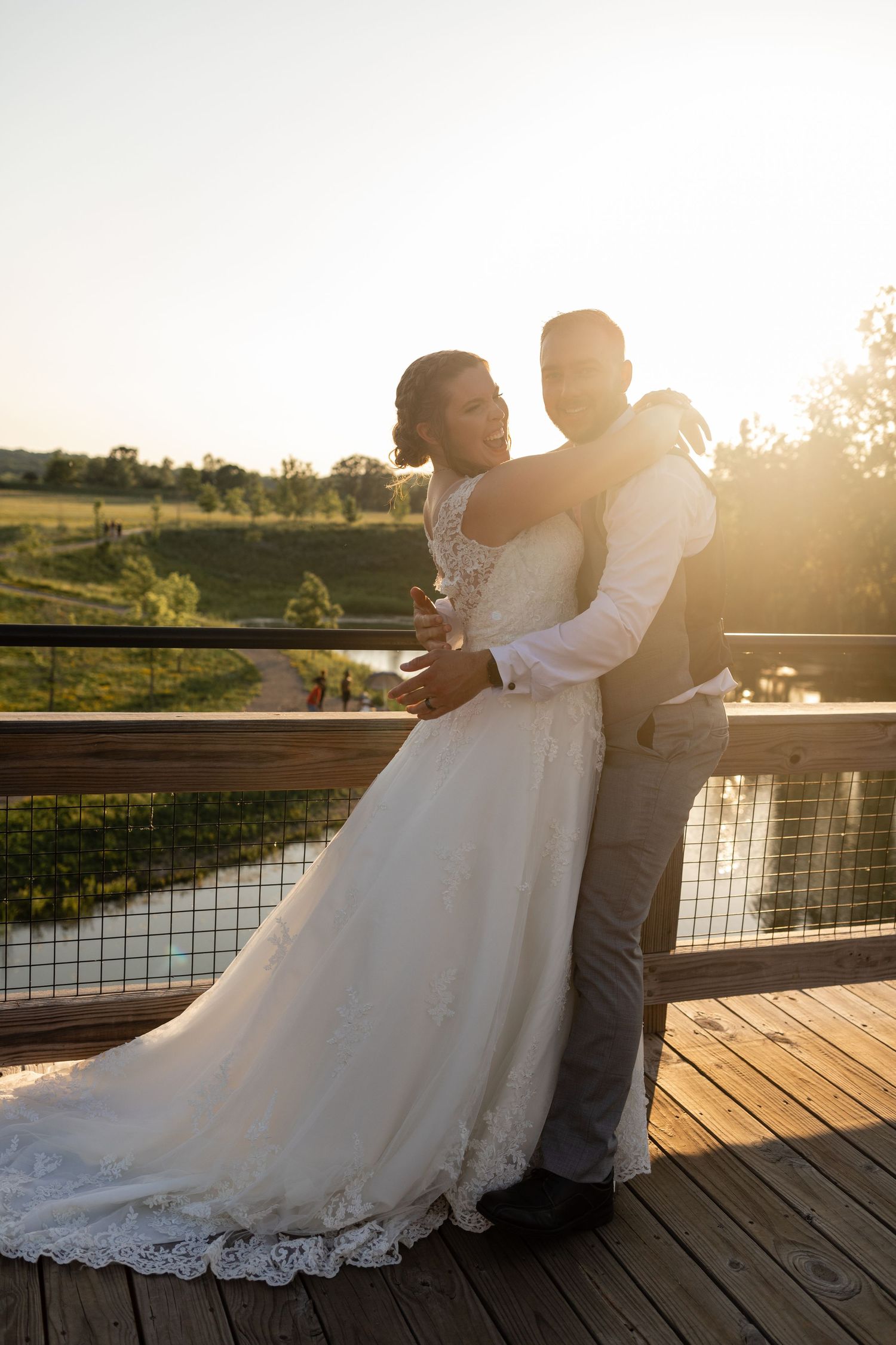 Bride and groom embracing on a deck at golden hour with scenic countryside views.