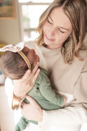 Parent holding sleeping infant in cozy cream sweater by window.