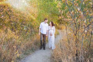 Couple walking hand in hand through autumn field at golden hour.