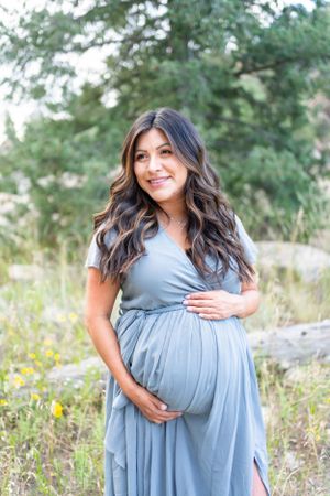 Joyful maternity portrait in flowing blue dress outdoors.