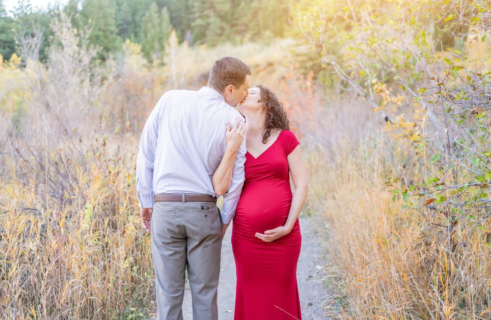 Romantic maternity photo of couple in sunlit field with tall grasses.