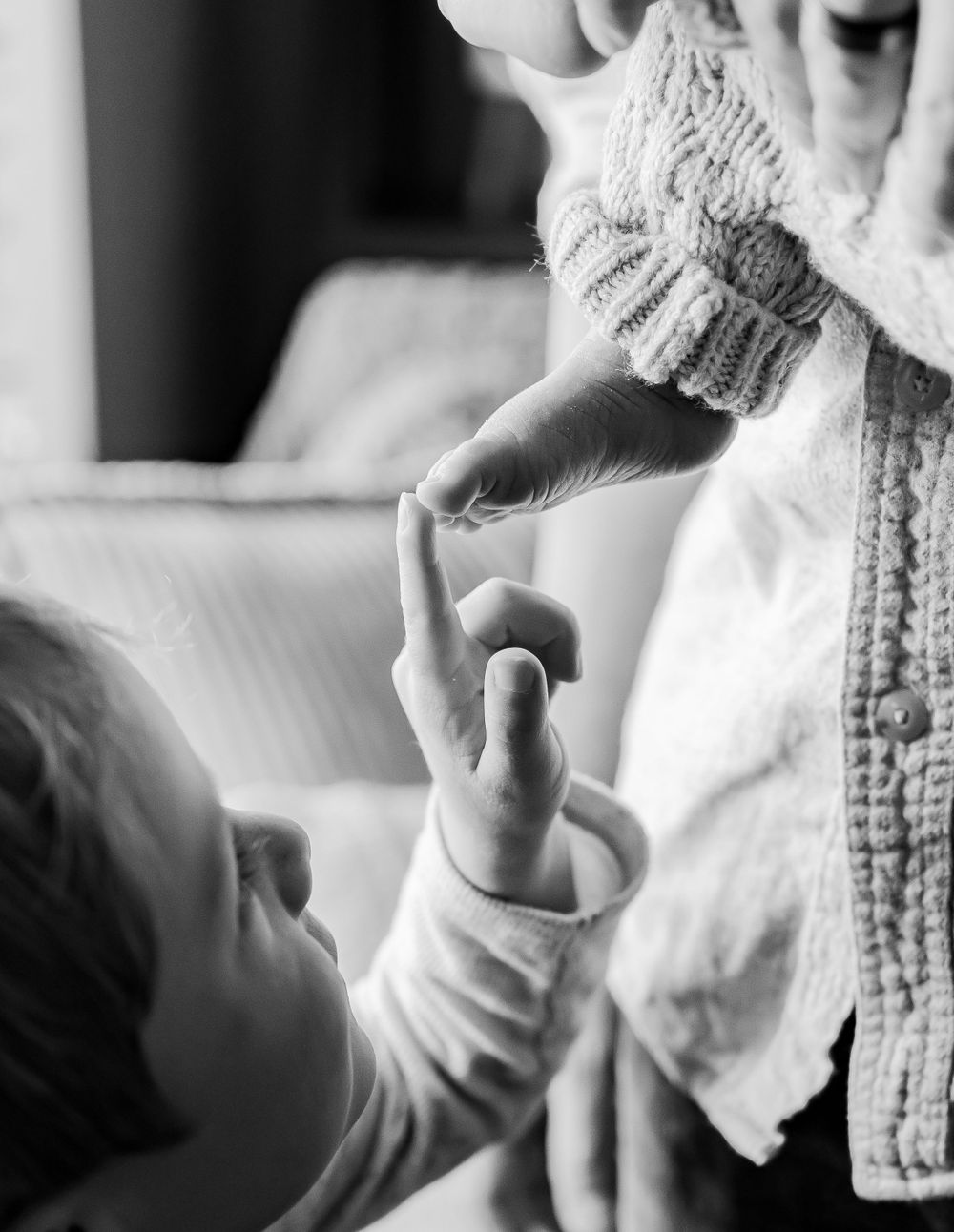 Black and white close-up of baby's hand reaching up in cozy sweater setting.
