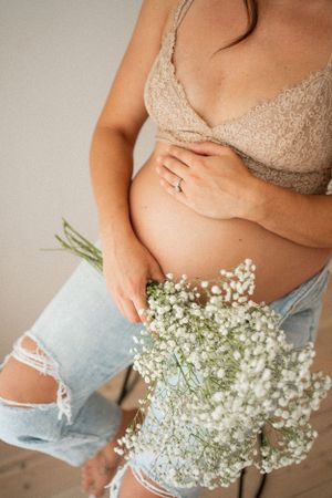 Close-up maternity photo with baby's breath flowers and distressed denim details.