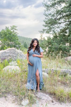 Maternity portrait in blue dress against mountain landscape.