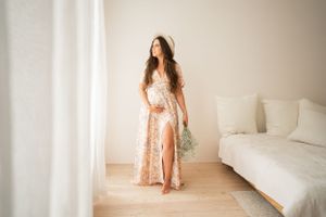 Elegant maternity portrait in a peach dress holding baby's breath flowers in bright indoor setting.