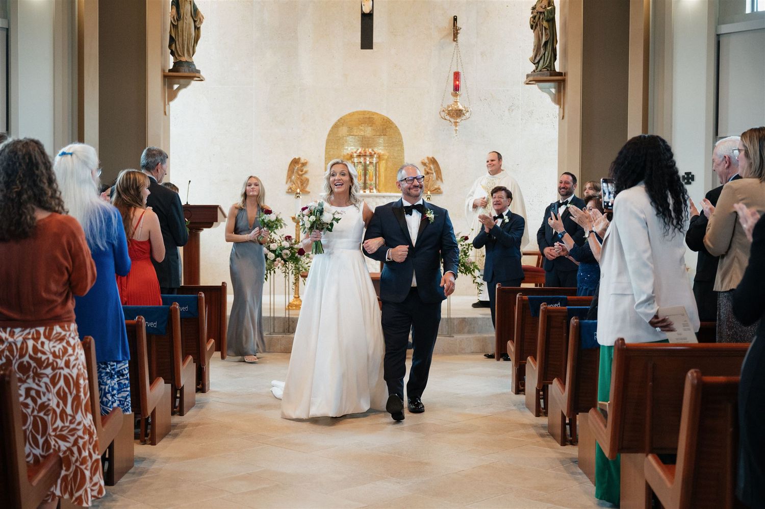Newlyweds walk down the church aisle while guests celebrate from the pews.