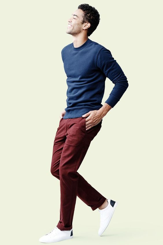 Man in navy sweater and burgundy pants striking casual pose against light background.