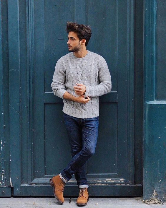 Street style photo of man in gray cable knit sweater and jeans against teal door.