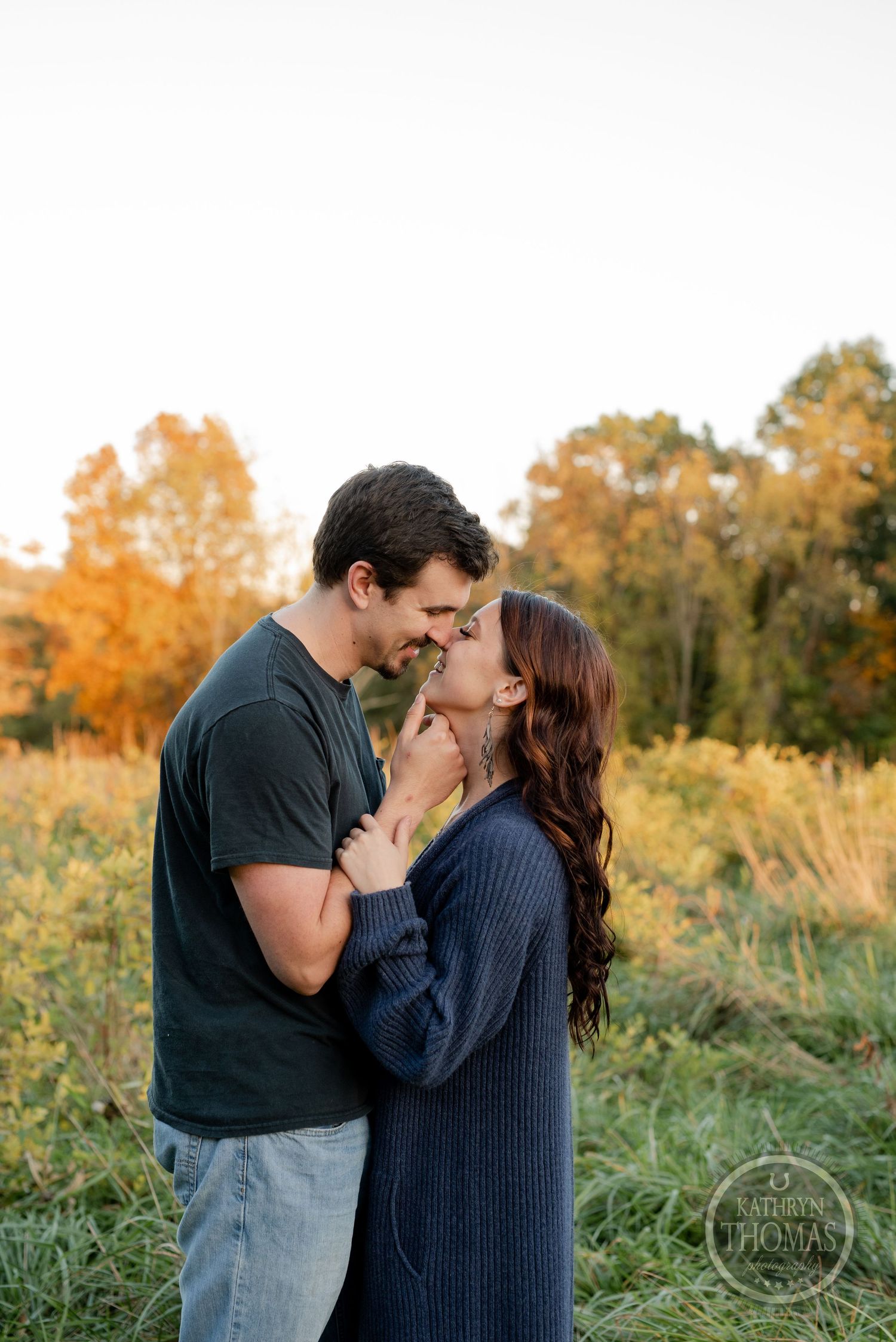 A tender embrace captured in a field with fall foliage in the background.