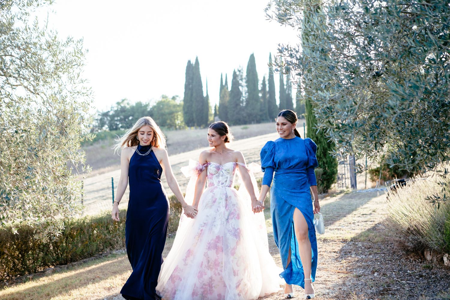 bridesmaids and bride hold hands and walk together as the sun sets in Tuscany
