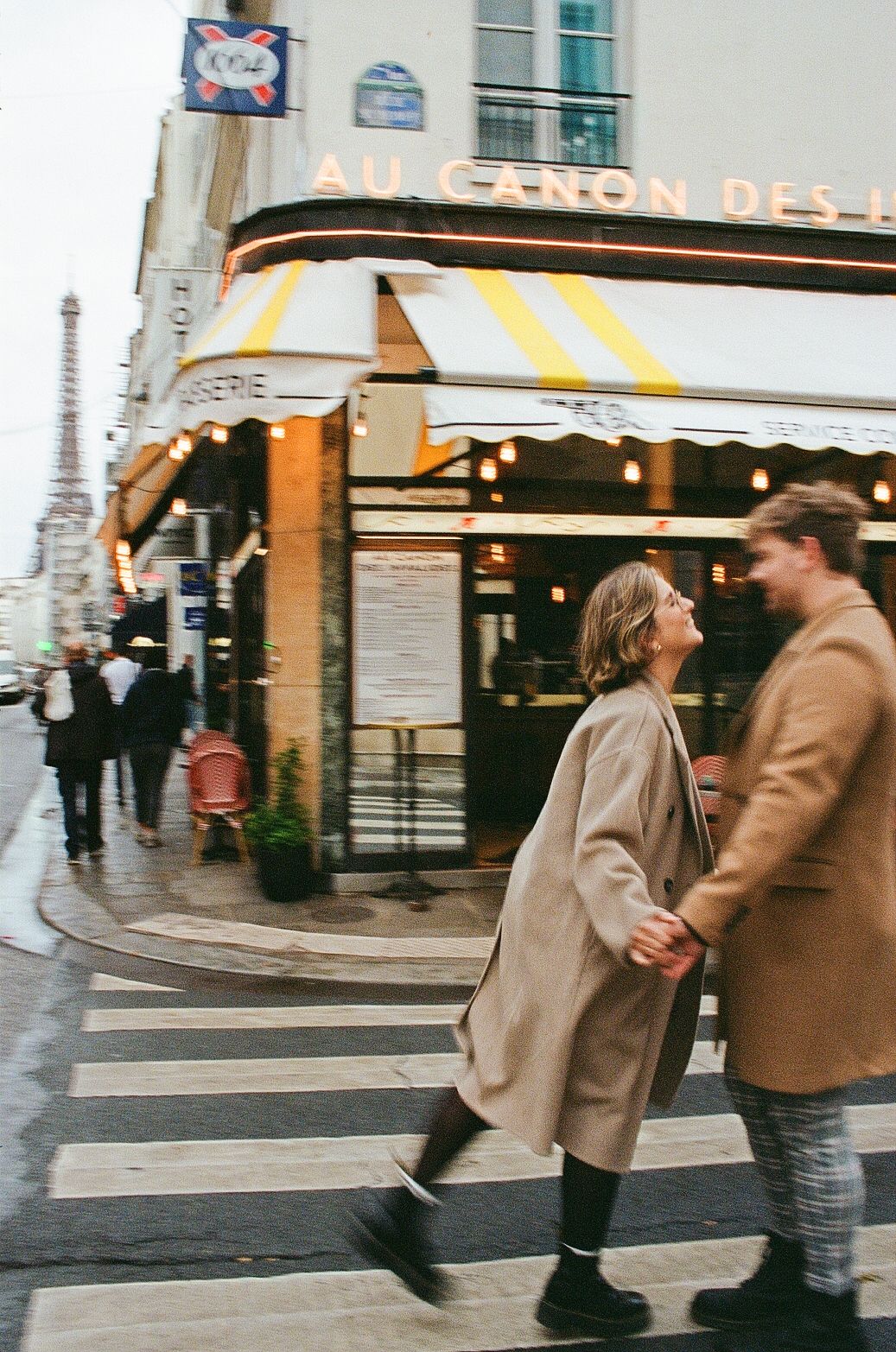 Couple in winter coats sharing a romantic moment outside a Parisian cafe on a street corner.