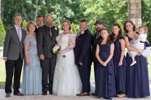 Wedding party poses outdoors in formal attire with bridesmaids in navy dresses and groomsmen in dark suits.