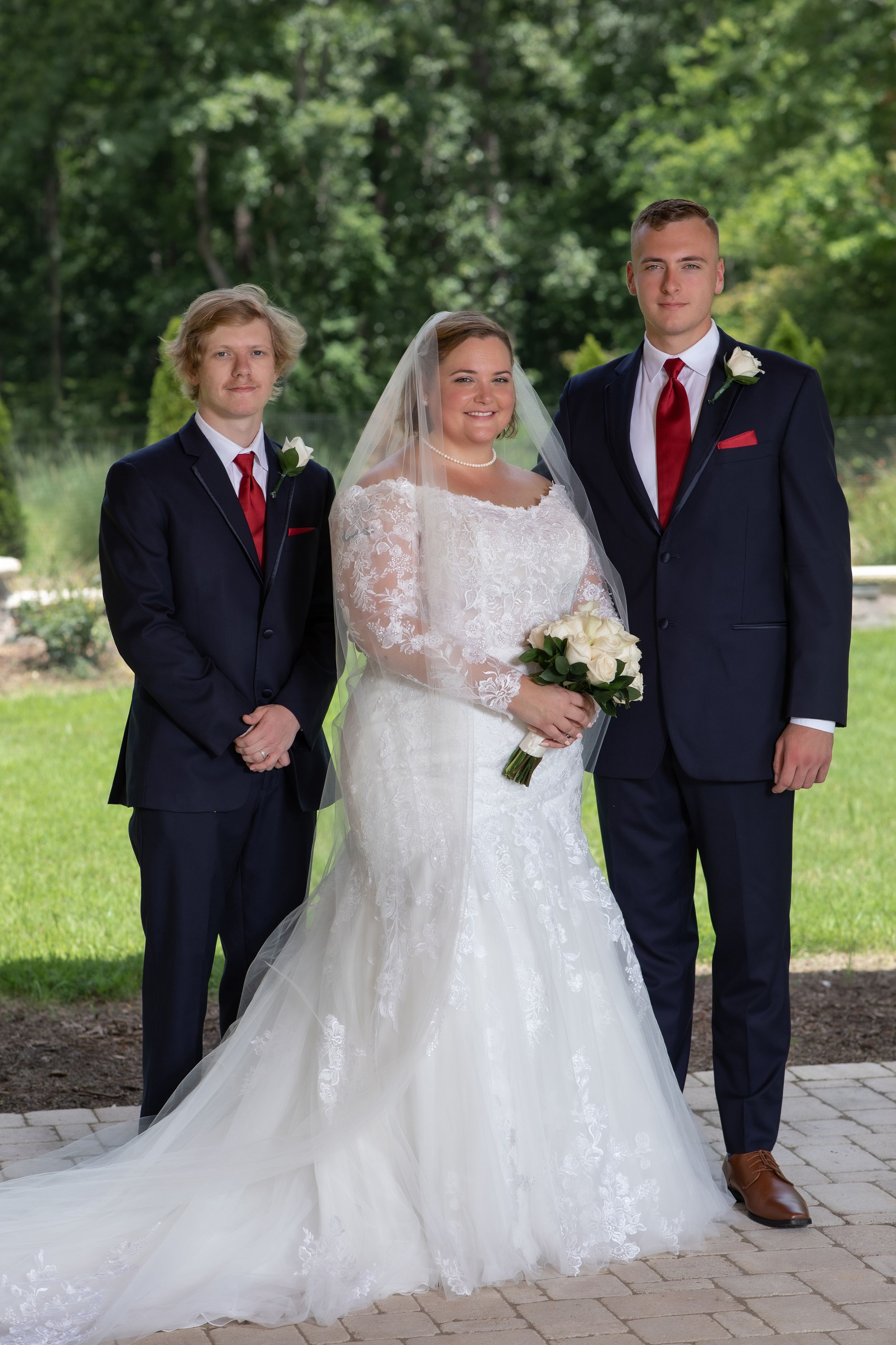 A wedding party poses on a stone path with groomsmen in dark suits with red accents.