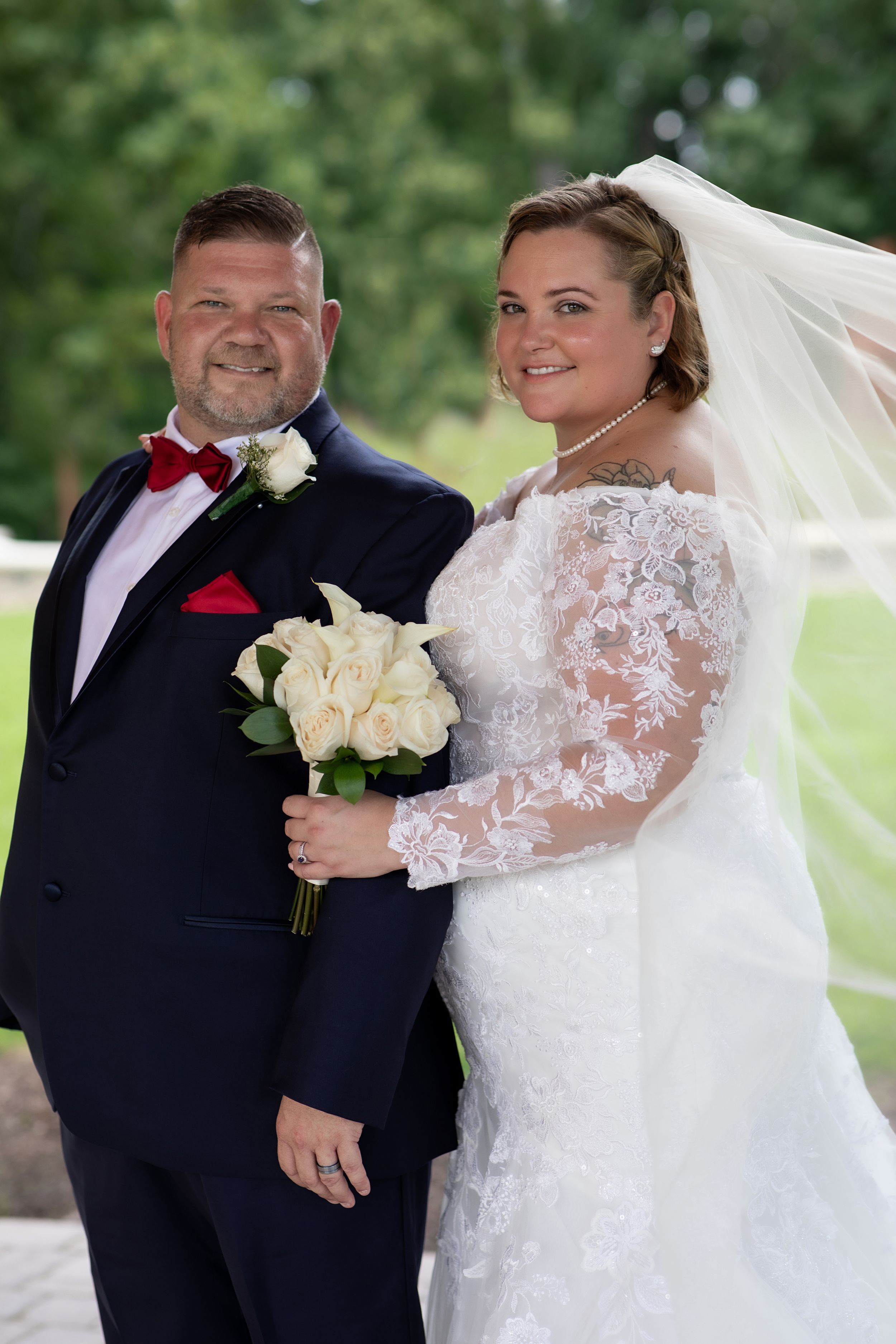 Wedding portrait of couple in navy suit and lace dress holding white rose bouquet.