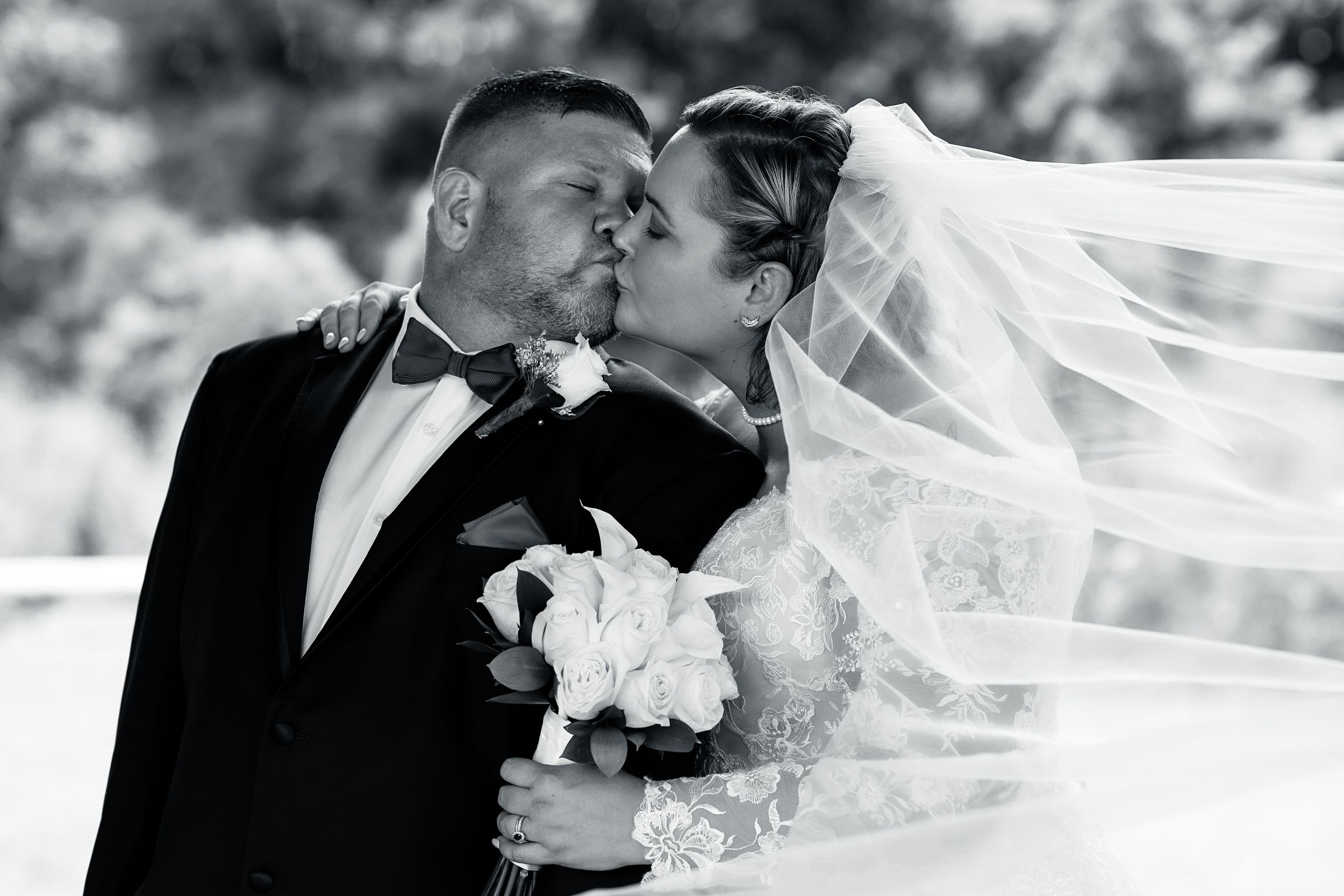Romantic black and white portrait of couple kissing with flowing veil and white bouquet.