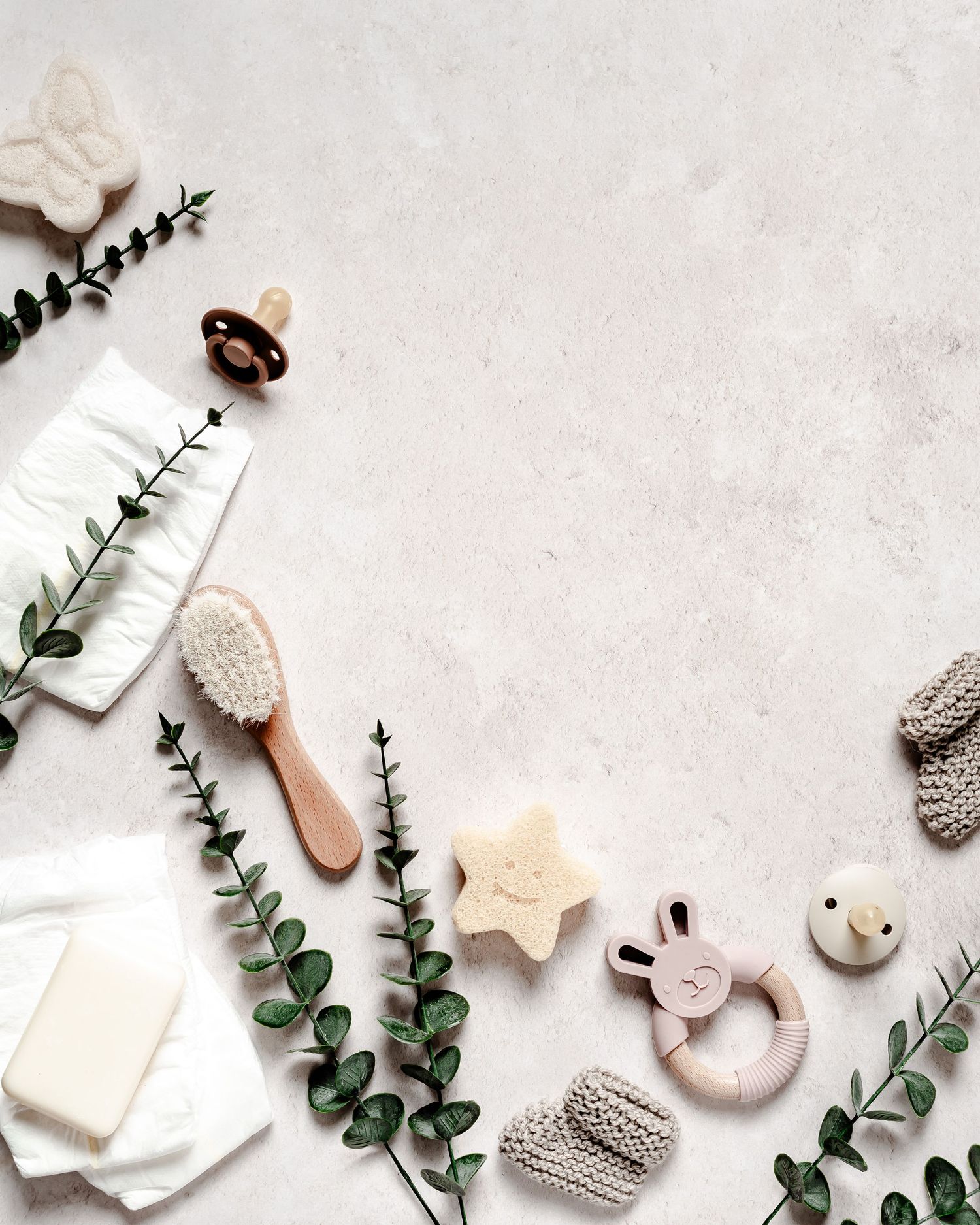 Baby accessories, nappies, dummies, brush, toys angled around a rustic flatlay background. Newborn, parents, children