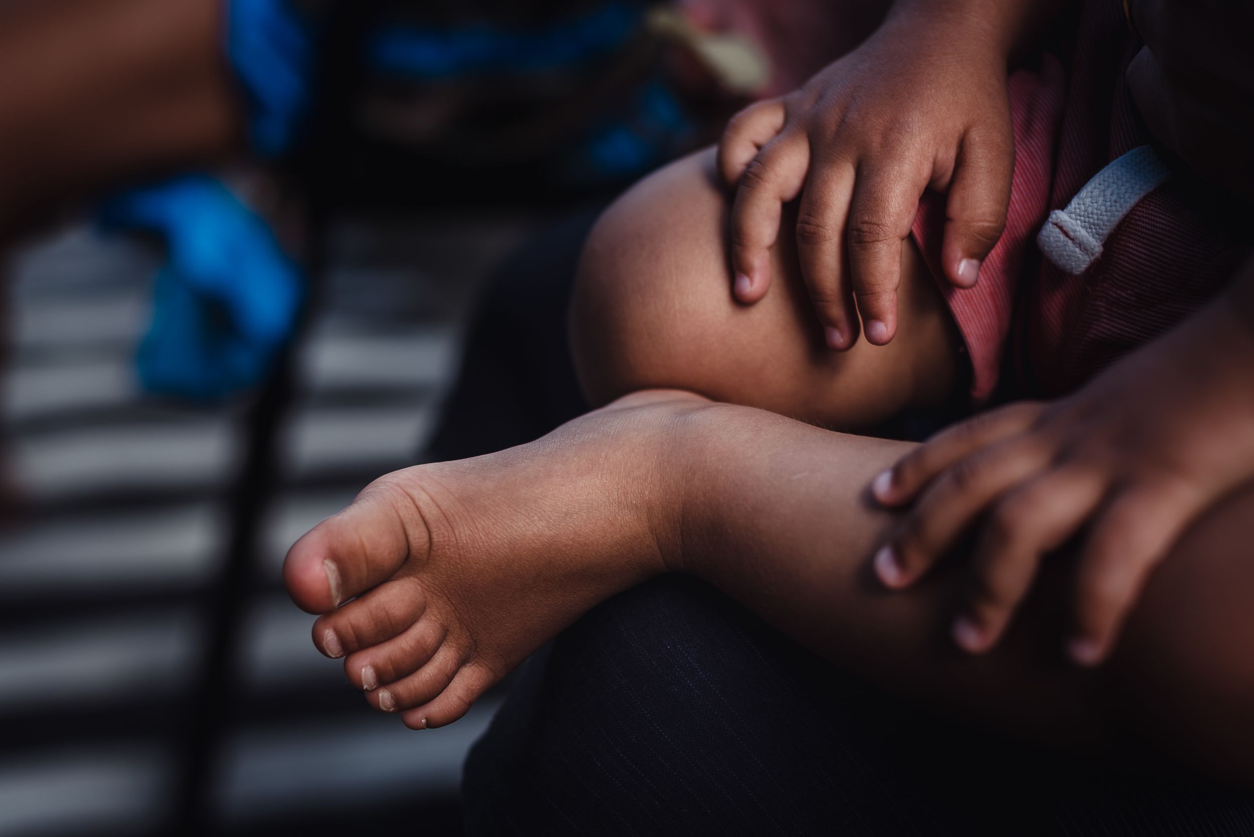 Close up image of a young child's feet as they sit on their mothers lap.