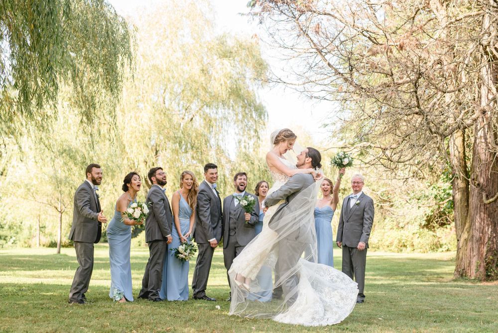 Fun photo of the groom lifting the bride, surrounded by the bridal party, capturing a joyful and playful moment