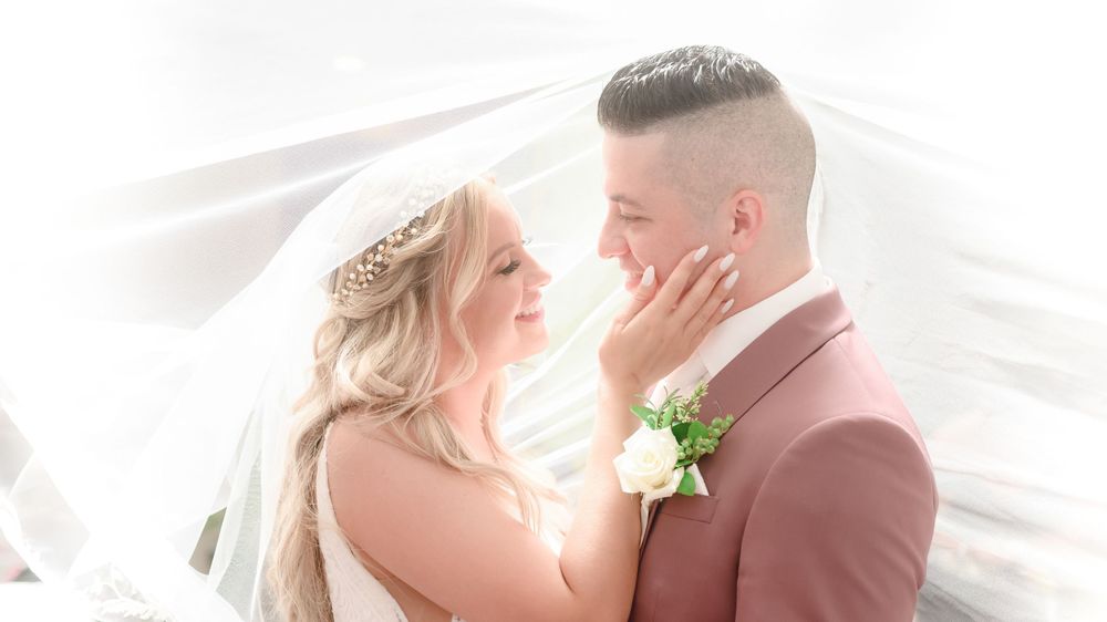 Intimate moment captured under the veil. Bride tenderly caresses groom's face.