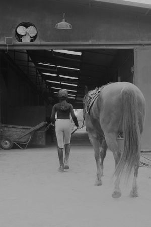 A black and white image of a horse and handler walking into a stable building.
