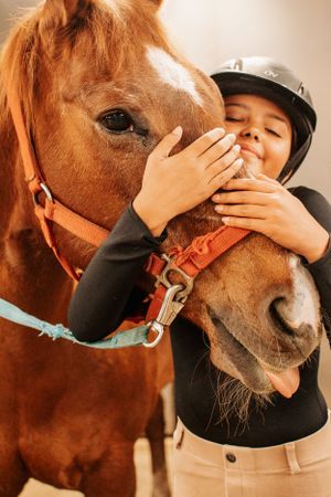 Close-up of chestnut horse and rider sharing an affectionate moment in riding gear.