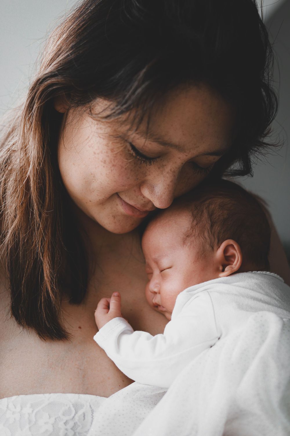 Freckled mother nuzzling her sleeping newborn baby with gentle affection.