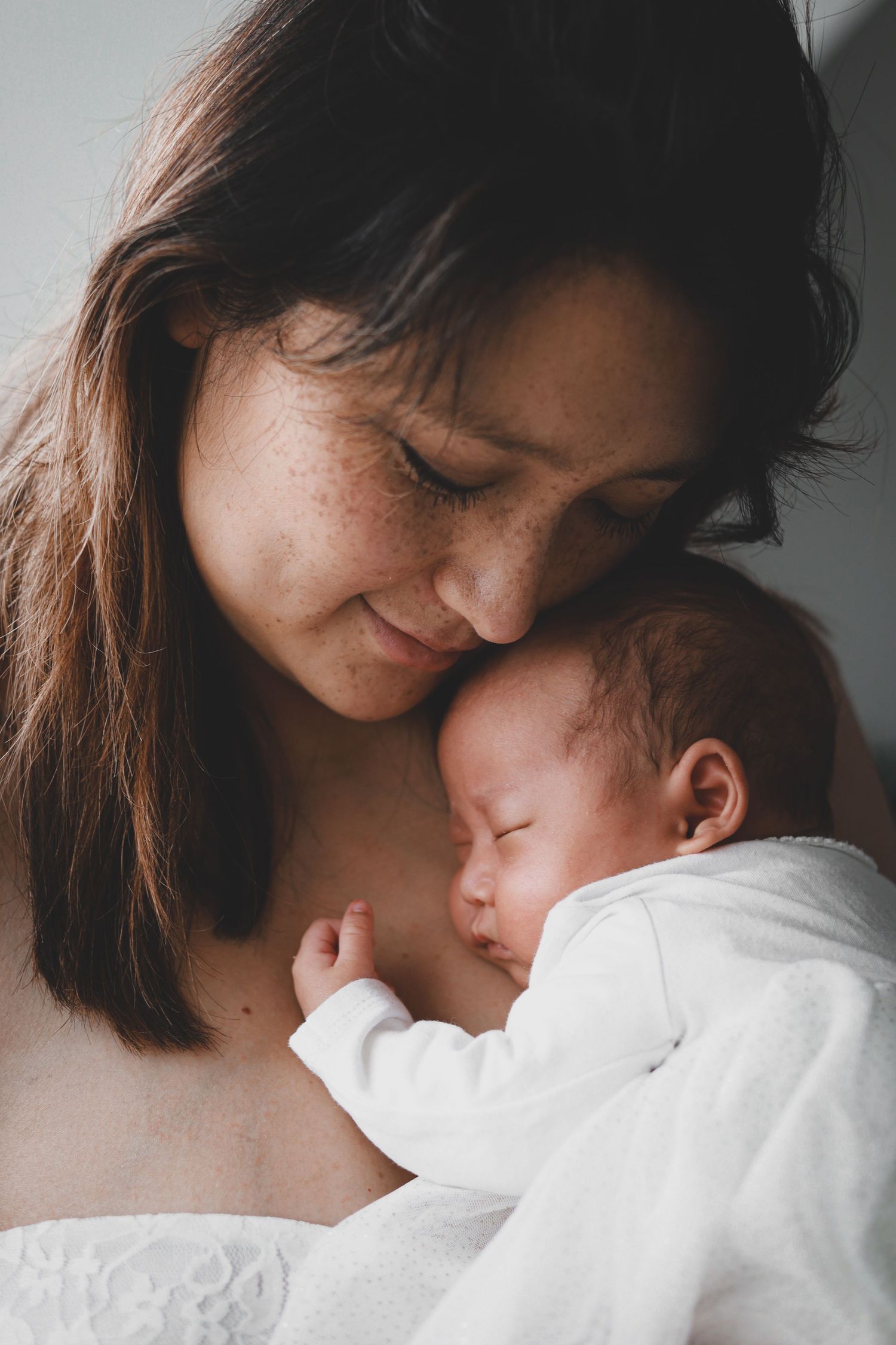 Freckled mother nuzzling her sleeping newborn baby with gentle affection.
